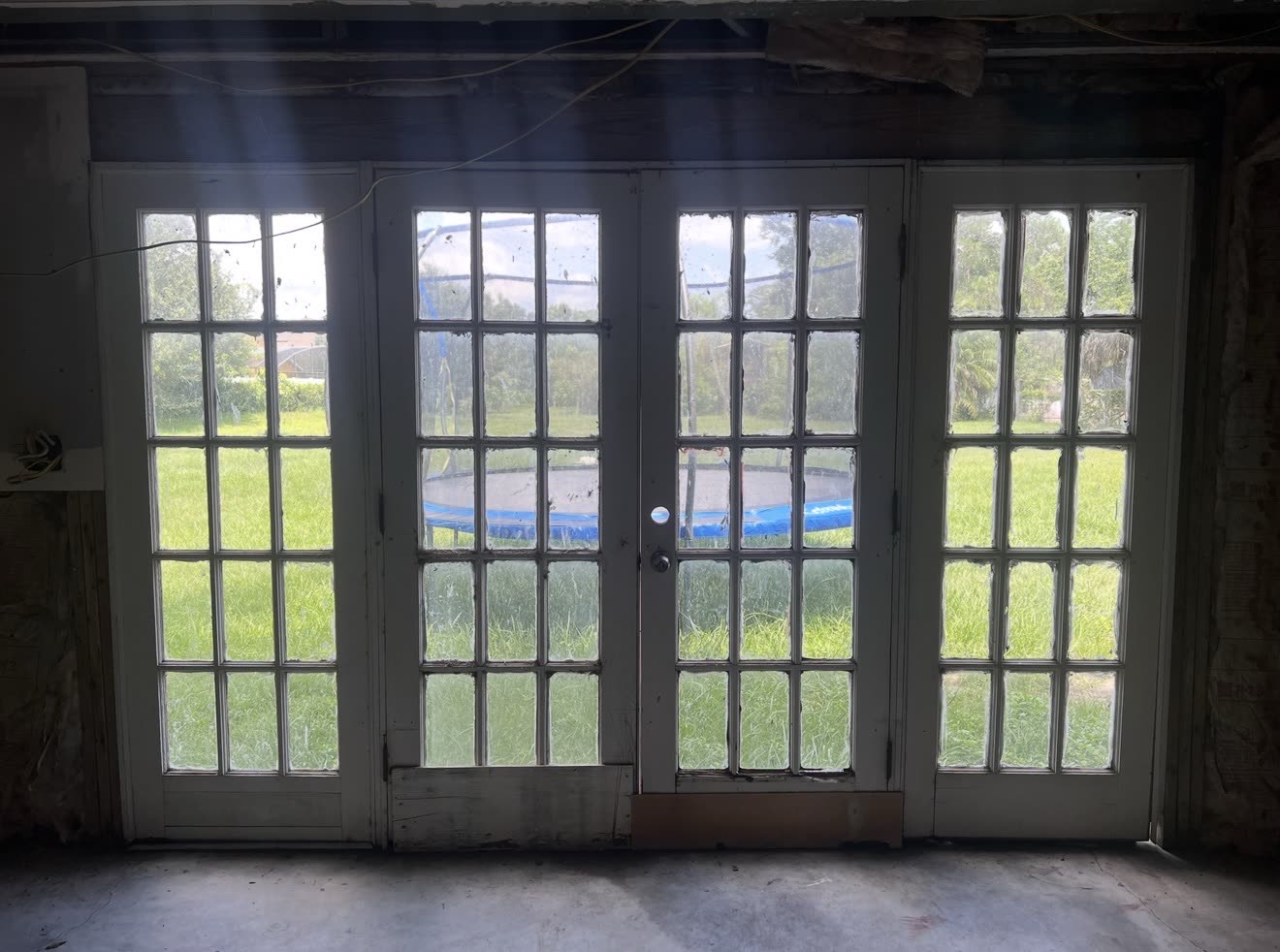 Old wood French doors with divided lites, fogged glass and a rotted bottom rail, in a room stripped back to the studs